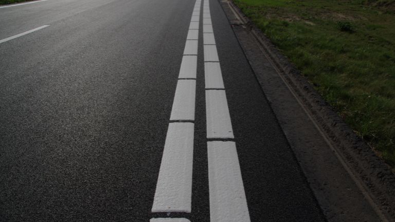 Close-up of a paved road with double white dashed lines on the right.